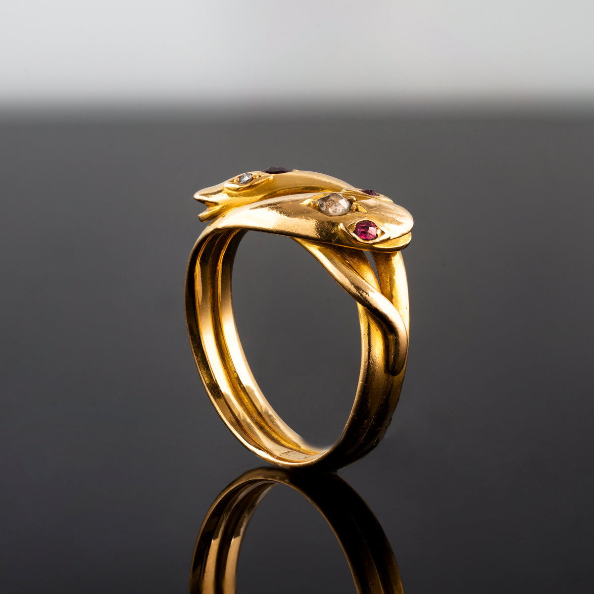 Side view of antique British snake ring with ruby and diamond details on black background.
