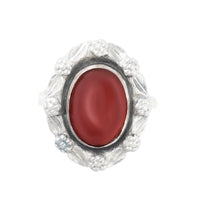 Front view of a 1930s Bernard Instone Arts and Crafts ring in 9ct gold and silver, set with an oval red carnelian cabochon and floral silver surround.