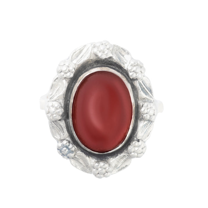 Front view of a 1930s Bernard Instone Arts and Crafts ring in 9ct gold and silver, set with an oval red carnelian cabochon and floral silver surround.