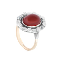 Angled side view of a Bernard Instone Arts and Crafts ring, showing the red carnelian cabochon in a silver leaf and flower setting on a 9ct gold band.