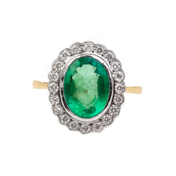 1930s emerald and diamond cluster ring in 18ct gold, featuring a vivid green emerald surrounded by old cut diamonds.