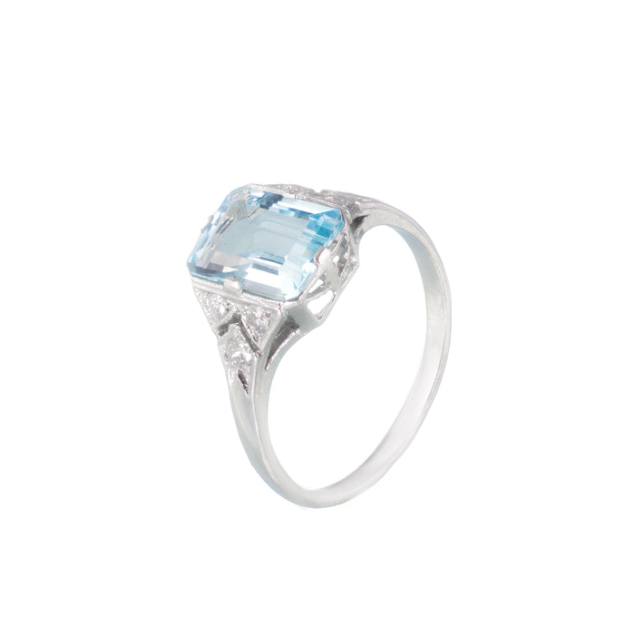 Angled view of vintage 1950s platinum ring featuring a 2.5ct emerald cut aquamarine, diamond shoulders, and pierced gallery detail.