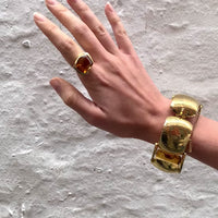 Large citrine cocktail ring worn on hand with chunky bracelet, 1960s gold setting with bold stone against a white wall