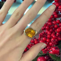 Close up of 1960s gold citrine ring worn on finger, geometric cut stone, against red berry's.