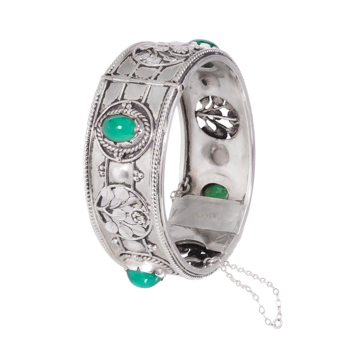 Side angle of 1930s Arts & Crafts silver and green chalcedony cuff bracelet showing floral repoussé details and safety chain.