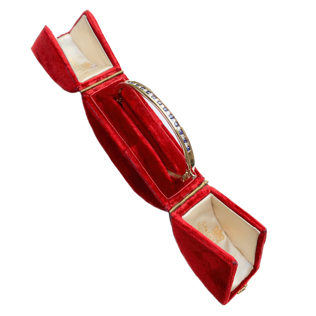 Side view of a vintage 1970s English 9ct gold sapphire and diamond bangle in a red display box.