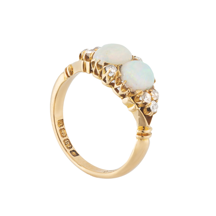 Side profile of a 1903 Edwardian ring with sculpted claw settings and twin opals flanked by bright antique-cut diamonds in a bold gold mount.