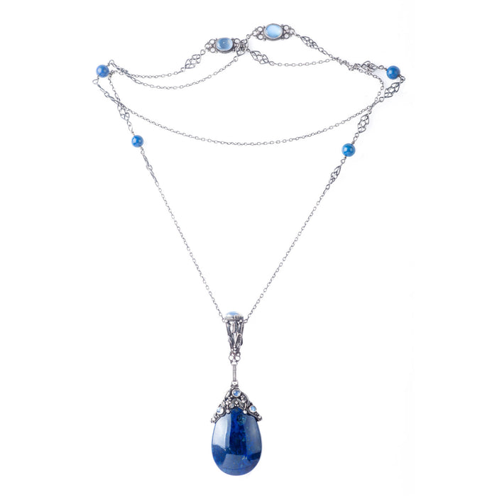 Full view of a long silver necklace by Amy Sandheim, showcasing intricate Arts & Crafts design with moonstone and lapis accents leading to a sculptural lapis pendant.
