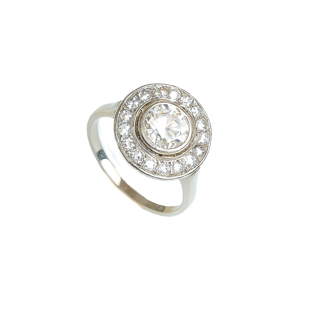 Angled view of French 1920s platinum diamond target ring with central old European cut diamond surrounded by millegrained halo of smaller stones.