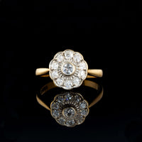 Antique diamond daisy cluster ring with old cut diamonds set in a scalloped platinum topped design on an 18ct gold band, reflecting softly against a dark surface.