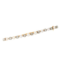 This image features a elegant Pearl & Diamond Bar Brooch. The brooch is crafted in eighteen carat gold and silver, showcasing a series of alternating cushion shaped old mine diamonds and white pearls.