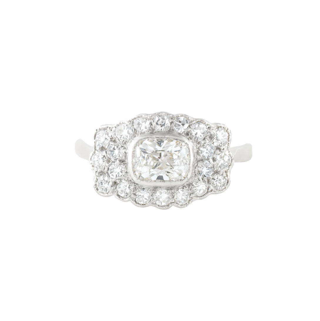 1940s diamond cluster ring in platinum with a cushion shaped old European cut centre diamond surrounded by single cut diamonds in a scalloped border.