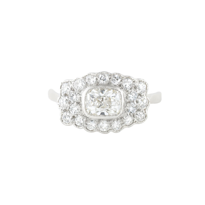 1940s diamond cluster ring in platinum with a cushion shaped old European cut centre diamond surrounded by single cut diamonds in a scalloped border.