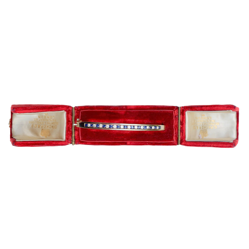 Vintage 9ct gold sapphire and diamond bangle, English c.1970s, shown in a red display box, front view.